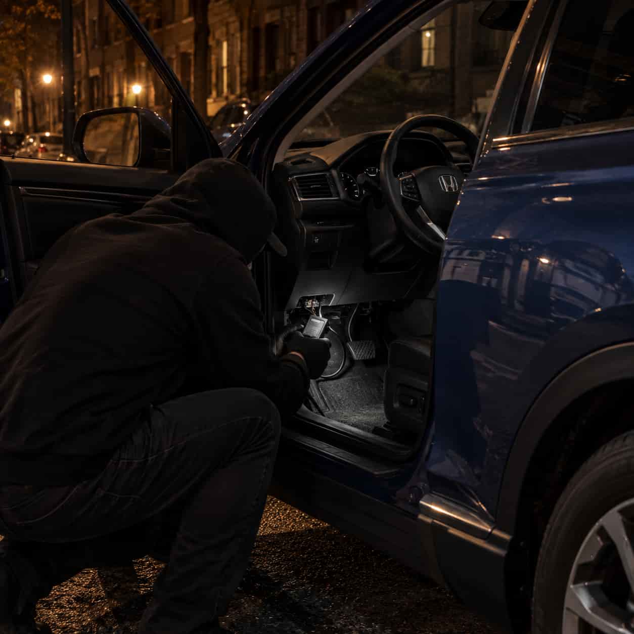 Thief plugging a programming device into the OBD port under a Honda's steering column